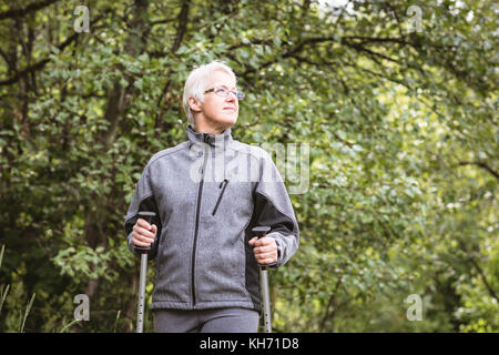 Senior woman hiker marcher avec des bâtons de marche dans la forêt Banque D'Images