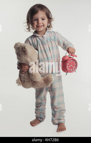 Portrait of little girl holding réveil et teddy bear toy, isolé sur fond blanc. Banque D'Images