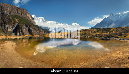 Vue magnifique avec de hautes roches avec des pics couverts de neige, lac de montagne, la réflexion dans l'eau, ciel bleu avec des nuages dans le lever du soleil. Le Népal. Magnifique vue panoramique Banque D'Images