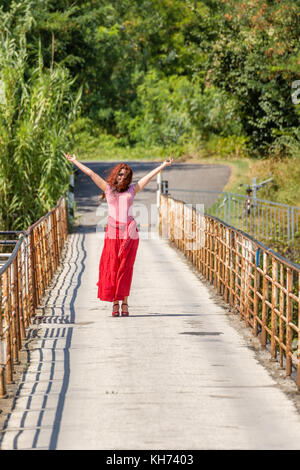 Red-haired girl irlandais marche sur un vieux pont de fer rouillé et raising arms Banque D'Images