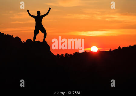 Randonnée homme silhouette en montagne, coucher de soleil et nuages. Randonneur grimpeur Homme bras tendus au-dessus de montagne après réussite à l'escalade à la beaut Banque D'Images