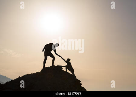 Couple d'équipe aide silhouette trust dans l'inspiration des montagnes. L'aide de l'équipe d'alpinistes l'homme et la femme randonneur, aider les uns les autres au sommet du mont Banque D'Images