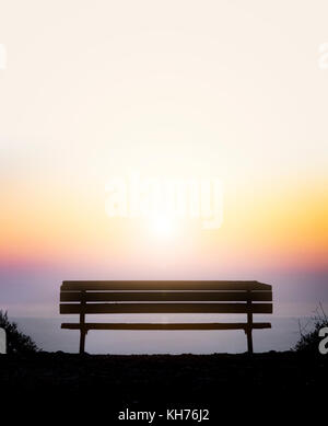 Vieux banc en bois donnant sur un coucher de soleil colorés au-dessus de l'horizon de l'océan brumeux Banque D'Images