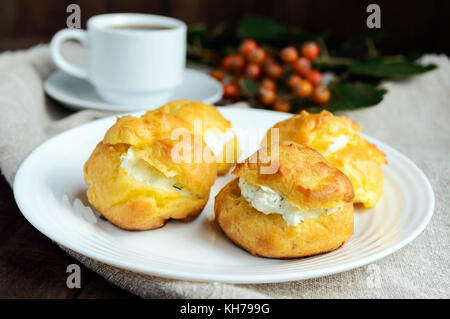 Des petits pains fraîchement cuits au four farcies éclairs épicé avec du fromage cottage et une tasse de café (espresso) sur un fond de bois foncé. petit-déjeuner léger. Banque D'Images