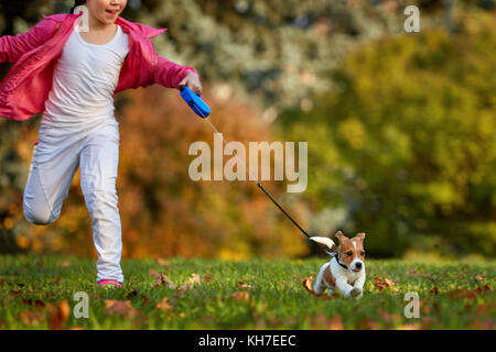 Girl s'exécuter dans un parc avec un chiot Jack Russell Terrier. heureux les amis à l'extérieur loisirs. Banque D'Images