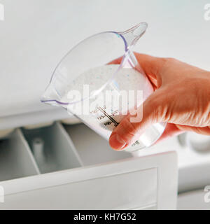 Main de femme qui se remplit de tasse de dosage de détergent dans la machine à laver Banque D'Images