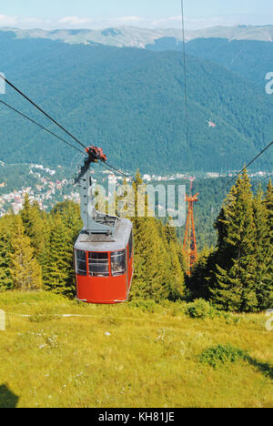 Vue de la cabine téléphérique rouge vif déménagement au sommet de la montagne au-dessus de beaux paysages avec des montagnes bleues, forêt, vallée verte et un à Banque D'Images
