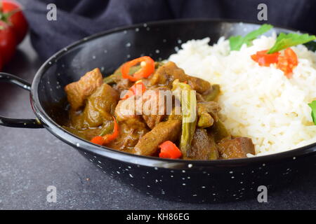 Porc au curry sauce épicée aux aubergines et haricots verts, servi avec du riz cuit dans un bol en métal noir sur un fond gris. La cuisine maison. Banque D'Images