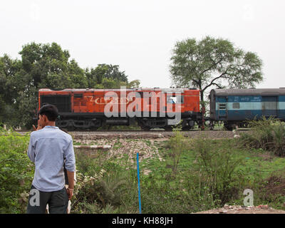 Une longue distance de voyageurs indiens train ralentit à l'approche d'un passage à niveau du chemin rural vu par un résident local Banque D'Images