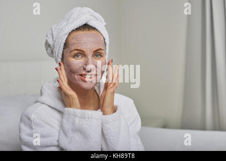 Femme dans un spa ayant un masque de beauté portant un peignoir blanc et coiffe smiling at the camera Banque D'Images