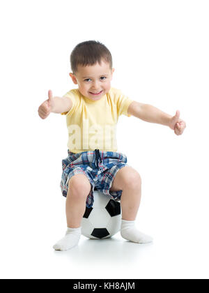 Enfant garçon est assis sur un ballon de soccer avec Thumbs up sign. Banque D'Images