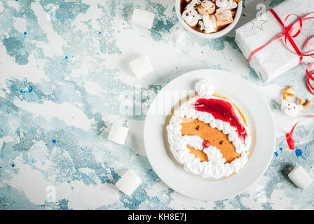 Idée pour un déjeuner de Noël pour les enfants : des crêpes décorées comme le père Noël, le cacao avec nounours et deer. guimauve sur un bleu clair backgroun Banque D'Images