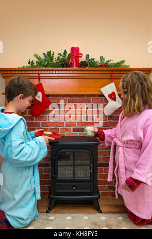 Deux enfants, un garçon et une fille, mettre un verre de lait et mince pie / cookie out pour le père Noël la veille de Noël. Banque D'Images