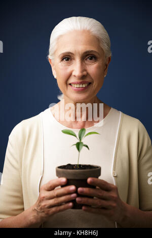 Photo en gros plan d'heureux de woman holding plante verte dans le spot, looking at camera, sur fond bleu foncé Banque D'Images