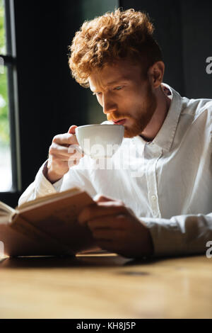 Close-up portrait of handsome giger homme barbu frisé café potable alors que reading book Banque D'Images