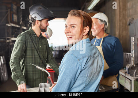 Jeune femme comme apprenti travailleur souriant avec joie dans l'atelier de métallurgie Banque D'Images