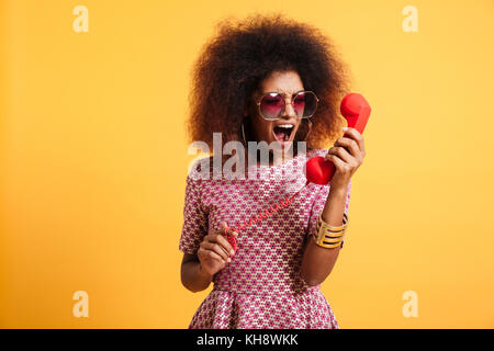 Portrait d'une femme en colère folle en rétro vêtements de style de crier sur fond jaune isolé téléphone Banque D'Images