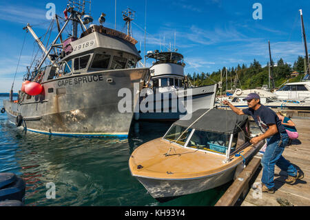 Femme enfilant un bateau sur la jetée, bateaux de pêche amarrés à la marina de Quathiaski Cove sur l'île Quadra, région de l'île de Vancouver, Colombie-Britannique, Canada Banque D'Images