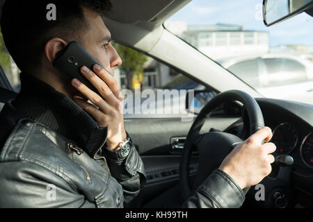 Jeune homme s'exprimant sur le téléphone portable en conduisant une voiture Banque D'Images