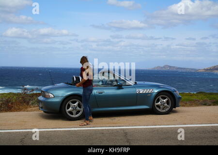 Une jeune femme qui monte dans une voiture de sport cabrio cabrio décapotable, vue panoramique sur la plage en arrière-plan. Banque D'Images