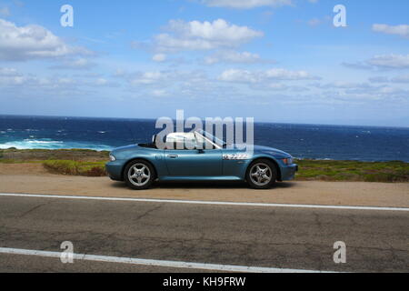 Une jeune femme heureuse assise dans une voiture de sport cabrio cabrio convertible, vue panoramique sur la plage en arrière-plan. Banque D'Images