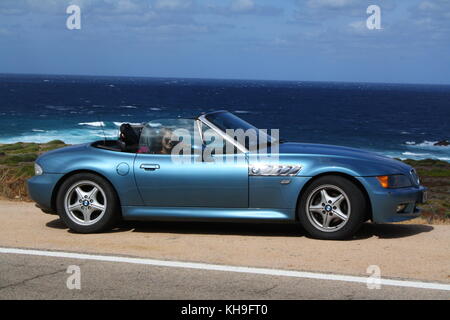 Une jeune femme heureuse assise dans une voiture de sport cabrio cabrio convertible, vue panoramique sur la plage en arrière-plan. Banque D'Images