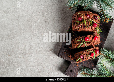 Le dessert traditionnel de Noël, bûche de Noël gâteau à la crème au chocolat, canneberges et romarin brindilles. sur fond gris en pierre avec noël tre Banque D'Images