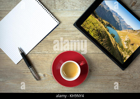 Tablette avec photo du lac dans les alpes, bloc-notes, stylo à bille et tasse de café Banque D'Images