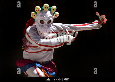 Tbetan moine dans un costume et un masque d'un squelette avec crânes blancs exécute une danse sacrée de tsam, close-up, un fond noir. Banque D'Images