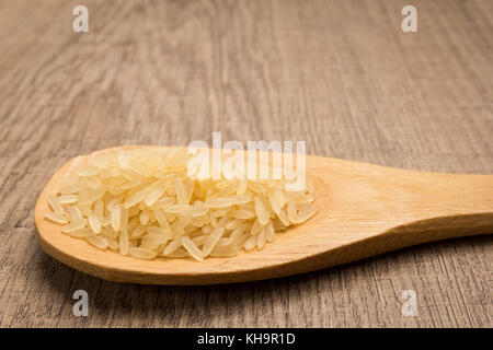 Oryza sativa est nom scientifique de semences de riz chinois étuvé. Également connu sous le nom de arroz agulha parboilizado (portugais). Les grains dans la cuillère en bois. rustique. Banque D'Images