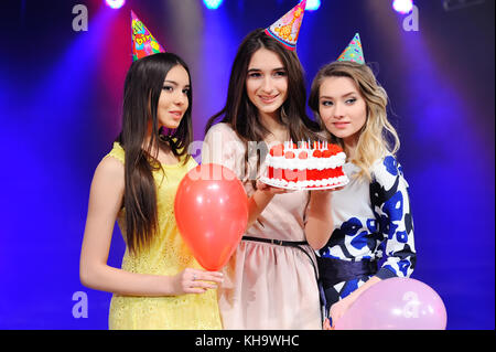 Trois jeunes filles dans des chapeaux et des ballons et des gâteaux dans la main. Banque D'Images