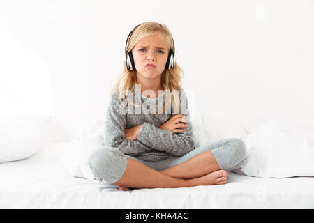 Les femmes en colère kid casque assis les bras croisés et les jambes au lit, looking at camera Banque D'Images