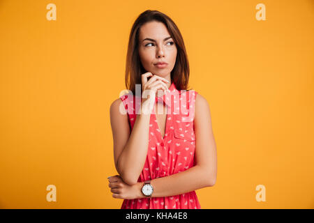 Portrait of beautiful brunette woman, toucher son menton, à côté, isolé sur fond jaune Banque D'Images