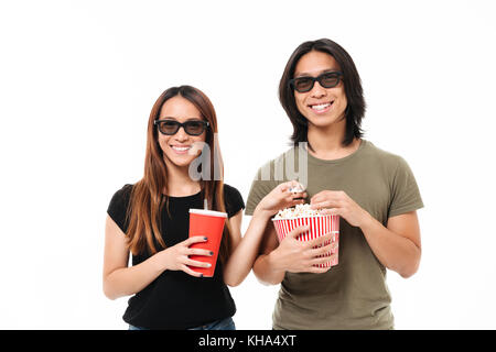 Portrait of a smiling young asian couple en 3D sans lunettes eating popcorn et cokenwhile potable looking at camera isolated over white background Banque D'Images