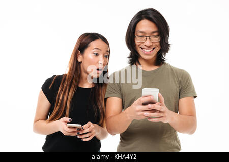 Portrait d'un jeune couple à l'aide de téléphones mobiles isolés sur fond blanc, une femme essaie de regarder son petit ami p Banque D'Images