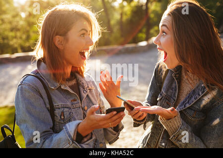 Deux heureux jeune brunette woman holding smartphones, se regarder en plein air parc Banque D'Images