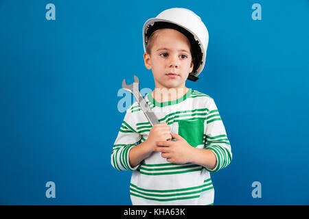 Ennuyer jeune garçon en posant avec casque de protection comme clé et ingénieur à l'écart sur fond bleu Banque D'Images