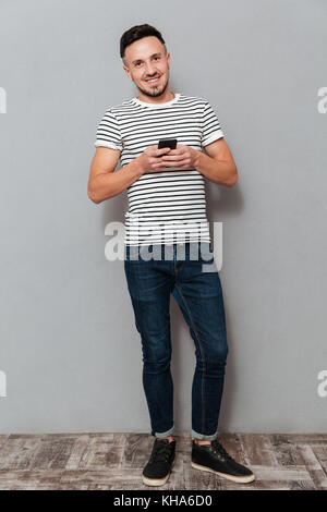 Longueur totale image of man holding smartphone et regardant la caméra sur fond gris Banque D'Images