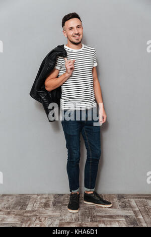 Longueur totale image of man holding sa veste sur l'épaule et regardant la caméra sur fond gris Banque D'Images