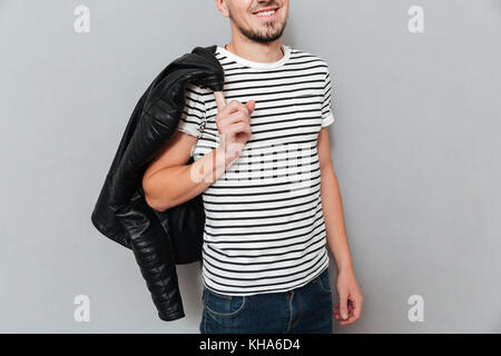 Portrait of smiling man holding sa veste sur l'épaule sur fond gris Banque D'Images