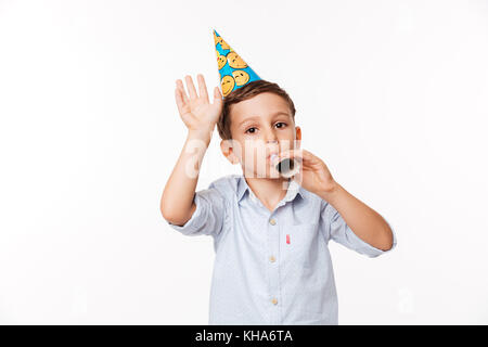 Portrait of a smiling cute little kid dans un chapeau d'anniversaire et de l'avertisseur sonore de soufflage looking at camera isolated over white background Banque D'Images