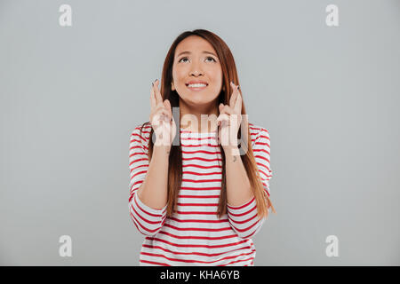 Portrait of a cute asian woman holding les doigts croisés pour la bonne chance et à la plus isolée de l'arrière-plan gris Banque D'Images