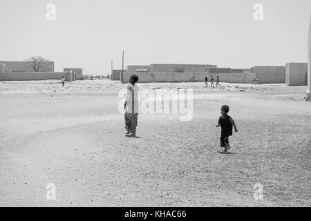 Deux enfants africains marcher dans un désert, village du Mali avec d'autres personnes dans l'arrière-plan. Banque D'Images