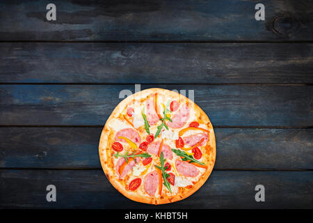 Délicieuse pizza au jambon, poivron, roquette, tomates et laitue iceberg sur un fond de bois foncé. Vue de dessus d'orientation bas Banque D'Images