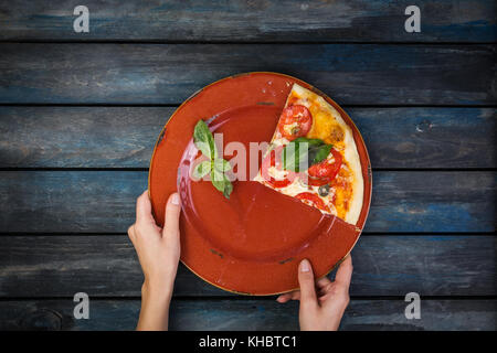 Woman's hands holding a plate avec deux morceaux de pizza margarita avec les tranches de tomates, les olives et les feuilles de basilic. sur un fond en bois foncé. vue d'en haut. Banque D'Images
