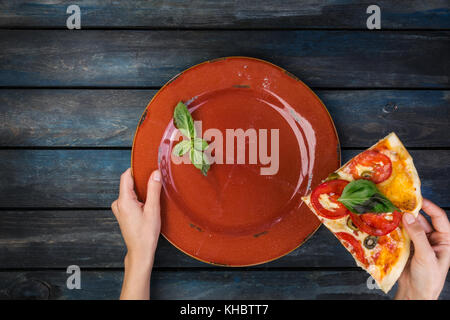 Woman's hands holding a plate avec deux morceaux de pizza margarita avec les tranches de tomates, les olives et les feuilles de basilic. sur un fond en bois foncé. vue d'en haut. Banque D'Images