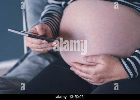 Femme enceinte en utilisant son smartphone pendant la grossesse Banque D'Images
