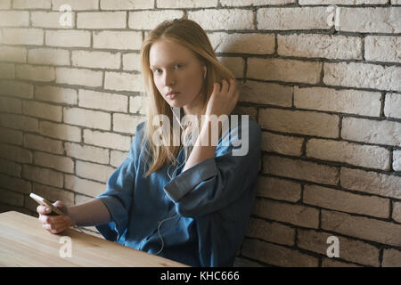 La fille est assise à la table dans les casques appuyé contre le mur, à la dépose de l'appareil photo dans les cheveux de son visage Banque D'Images