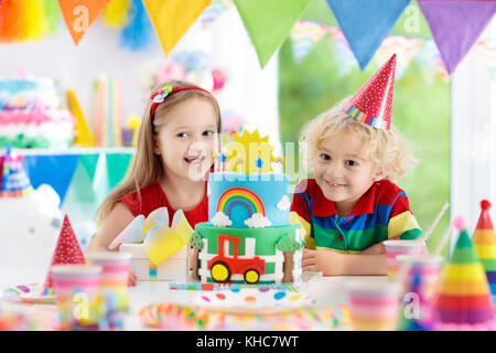 Kids Birthday party. child blowing out candles on cake coloré. Décoration maison avec des bannières drapeau arc-en-ciel, des ballons, des confettis et de les transporter à la ferme. Banque D'Images