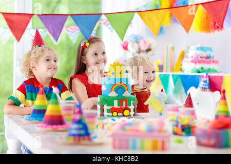 Kids Birthday party. child blowing out candles on cake coloré. Décoration maison avec des bannières drapeau arc-en-ciel, des ballons, des confettis et de les transporter à la ferme. Banque D'Images